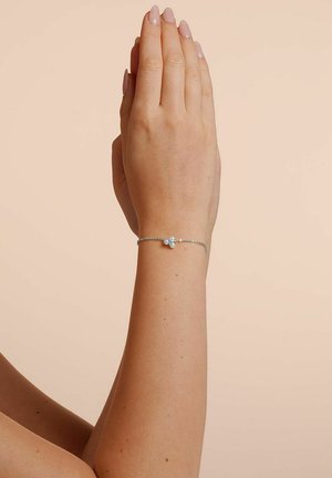 Silberne Kettenarmband mit drei kleinen dekorativen Perlen. Die Ansicht zeigt eine Hand mit in einem hellen Rosaton lackierten Nägeln.