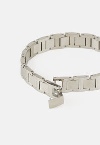Bracelet en acier inoxydable argenté avec des maillons rectangulaires, finition polie, et un fermoir portant les initiales "CK". Conçu de manière équilibrée, sans embellissements.