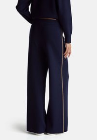 Granatowe spodnie o szerokich nogawkach wykonane z miękkiej dzianiny, z złotym paskiem po boku, elastyczną talią i luźnym krojem.