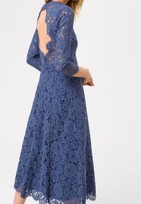 Vestido azul de encaje con mangas tres cuartos, patrón floral y diseño de ojo de cerradura en la parte posterior. Largo midi con acabado de dobladillo en forma de scallop.
