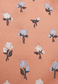 Bomullstyg i korall med broderade blommor. Blommorna är i blått, vitt och svart, med detaljerade kronblad och blad.