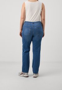 Jeans de mezclilla azul claro con cintura alta, corte recto y dos bolsillos traseros, combinados con una blusa sin mangas blanca y zapatillas plateadas.