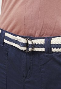 Pantalon bleu marine avec une ceinture tissée présentant des rayures bleu marine et crème, maintenue par une boucle métallique ronde, mettant en valeur une texture de tissu lisse.