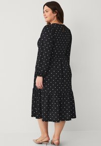 Vestido negro con lunares, de manga larga, con la cintura ajustada y dobladillo con volantes. Tejido ligero con una apariencia texturizada y detalle de ojal en la espalda.