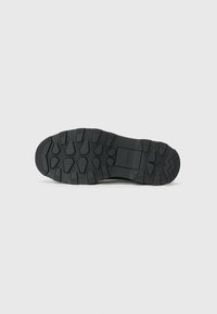 Black rubber outsole featuring multi-directional traction lugs, flat profile, and a textured surface for enhanced grip on various terrains.
