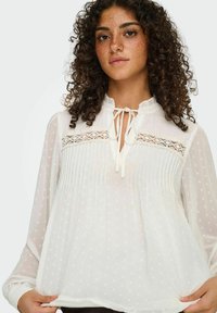 Hvid, gennemsigtig bluse med en rynket krave, nøglehulåbning med bånd, lodrette plisseringer og textured hjerte mønstre overalt.