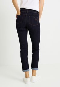 Vaqueros de mezclilla oscura con ajuste slim, puños doblados y costuras en contraste. Cuentan con dos bolsillos traseros y cintura de altura media.