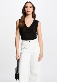 Top in maglia nera con collo a V e design testurizzato, abbinato a pantaloni bianchi a gamba larga con tasche frontali e dettagli dorati.