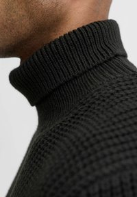 Zwarte gebreide coltrui met een textuurpatroon en een geribbelde kraag. Close-up weergave legt de nadruk op de stof en het detail van de kraag.