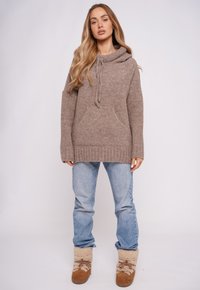 Beżowa dzianinowa bluza z kapturem ze sznurkiem, przednią kieszenią i ściągaczami na mankietach, zestawiona z jasnoniebieskimi dżinsami i beżowymi botkami wyściełanymi futerkiem.