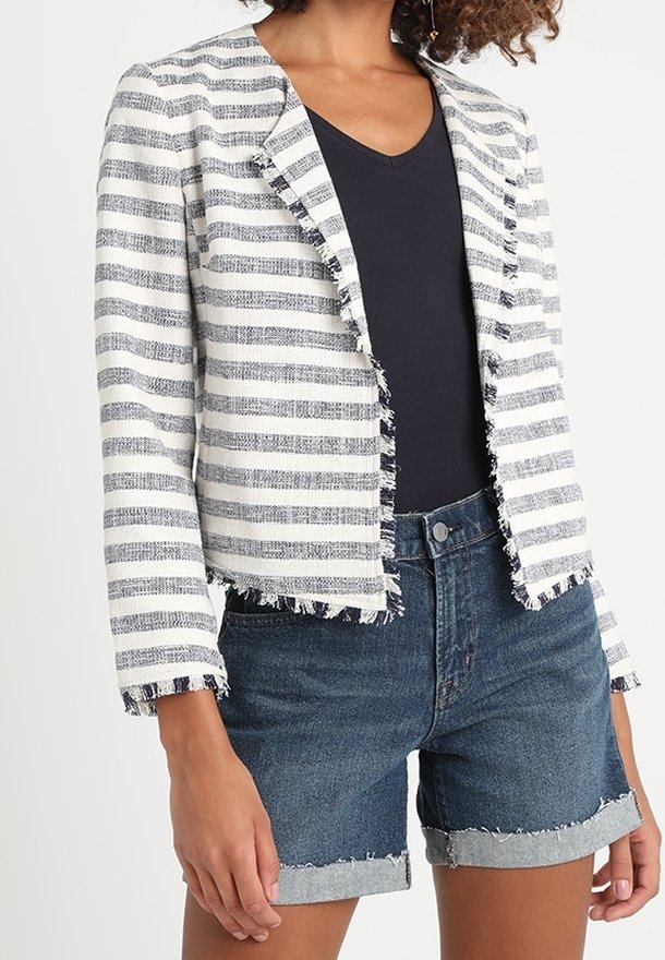 Blazer a righe bianco e blu navy, realizzato in tessuto testurizzato con bordi sfrangiati. Abbinato a pantaloni corti in denim a vita alta.