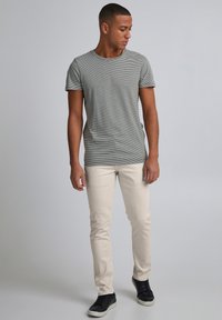 Tricou cu mânecă scurtă în dungi gri și albe, asortat cu blugi subțiri de culoare bej deschis și adidași negri, având un design simplu și casual.