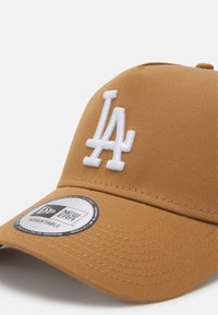 Casquette réglable marron en tissu texturé avec un logo "LA" brodé en blanc à l'avant et une étiquette circulaire New Era sur la visière.