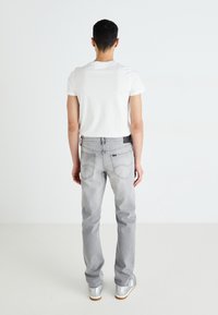 Γκρι τζιν παντελόνι σε ίσια γραμμή, πεντάτσεπη σχεδίαση και ραφές, συνδυασμένο με λευκή βαμβακερή μπλούζα και ασημένια αθλητικά παπούτσια.