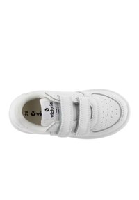 Zapatilla blanca de cuero con dos correas de velcro, perforaciones circulares en la puntera, cuello acolchado y suela de goma texturizada.