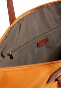 Oranje draagtas interieur met een gladde stoffen voering, voorzien van een ritsvak en een bruine leren label met de merknaam erop gedrukt.