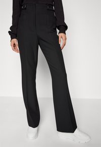 Svarta skräddarsydda byxor i ett slätt tyg med hög midja, med framfickor och subtila sömdetaljer. Matchade med vita sneakers.