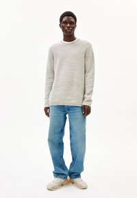 Hellgrau strukturiertes Sweatshirt mit Rundhalsausschnitt, kombiniert mit hellblauen Straight-Leg-Jeans und mehrfarbigen Sneakers.