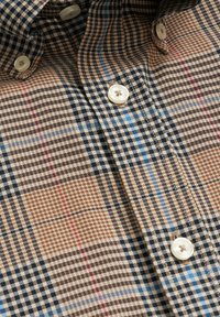 Een overhemd met knopen in een meerkleurig ruitpatroon met bruin, zwart en blauwe accenten. Zachte stof met witte knopen en een klassieke kraag.