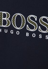 Granatowy materiał z wyraźnym napisem "BOSS" w białej czcionce, z żółtymi, przekątnymi pasami na literze "O", a poniżej napis "HUGO BOSS".