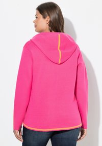 Rosa Kapuzenpullover mit gefütterter Kapuze und kontrastierendem orangem Stich, im lässigen Schnitt und mit gerippten Bündchen. Weicher Stoff ohne sichtbare Muster.