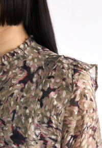 Blusa floreale con scollatura a volant e dettagli sulle spalle. Presenta un motivo multicolore in verde, rosa e nero su un tessuto leggero.