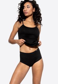 Top in cotone nero senza maniche con spalline sottili abbinato a mutande in cotone nero a vita alta. Entrambi i pezzi presentano una texture liscia e cuciture minime.