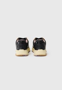 Black athletic shoes with a textured finish, featuring a beige sole, pink accents, and embossed "HUGO" logo on the heel.