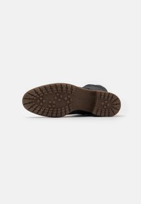 Bota negra con una suela de goma texturizada que presenta profundos surcos para una mejor tracción. La suela es de color marrón y la parte superior es lisa y redondeada.