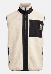 Gilet in felpa color crema con dettagli neri, colletto alto, zip frontale e tasche laterali. Una tasca sul petto presenta un piccolo logo.