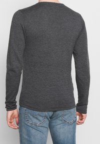 Langärmliges graues Shirt aus weichem Stoff, mit Rundhalsausschnitt, schlanker Passform und gerippten Bündchen, kombiniert mit blauen Jeans.