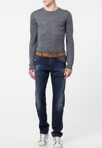 Grå långärmad tröja med ficka, i kombination med blå jeans och ett brunt läderbälte. Vita sneakers fulländar outfiten.