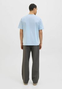 Lyseblå bomulds t-shirt med rund hals, korte ærmer, parret med løstsiddende mørkegrå bukser, der har et enkelt design.