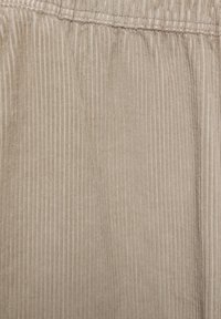 Barna kordbársony anyag finom függőleges csíkokkal, puha tapintású és elasztikus derékrésszel. Közeli felvétel a bordázott mintázatról és az anyag mélységéről.