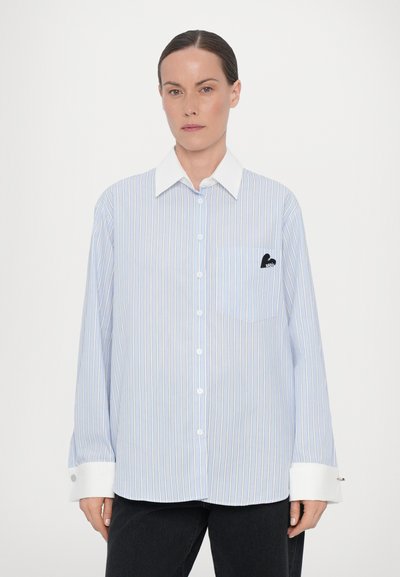 Light blue striped shirt with a white collar and cuffs. Features a pocket with a small black logo. Long sleeves and button closure.