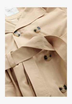 Gabardina beige con textura, que presenta grandes botones redondos moteados y un cinturón a juego. Diseño clásico con solapa y pliegues.