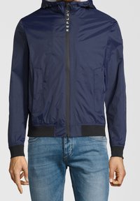 Giacca zip con cappuccio blu navy con polsini e vita neri, indossata con jeans azzurri, mostrata dalle spalle ai fianchi.