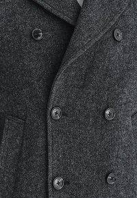 Ciemnoszary, wełniany płaszcz w jodełkę o podwójnym zapięciu, z dużymi czarnymi guzikami i kołnierzem z wycięciem.