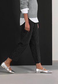 Bocanci argintii cu toc plat, asortați cu pantaloni negri cu buline albe și un pulover gri peste o cămașă albă.