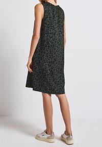 Tmavě zelené bezrukávové šaty s leopardím vzorem, s kulatým výstřihem a volným střihem, doplněné o lehké tenisky.