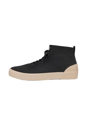 Zapatilla deportiva de punto negra de caña alta con suela de goma beige y cordones, mostrada de perfil sobre un fondo blanco.