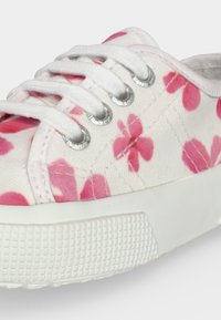 Hvid lærredssneaker med pink blomsterprint, hvide snørebånd, metaløjer og tyk tekstureret hvid gummisål.