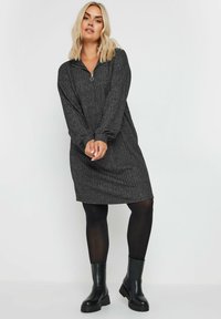 Abito maglione grigio, testurizzato, con colletto a quart di zip e maniche lunghe, abbinato a leggings neri e stivali neri robusti.