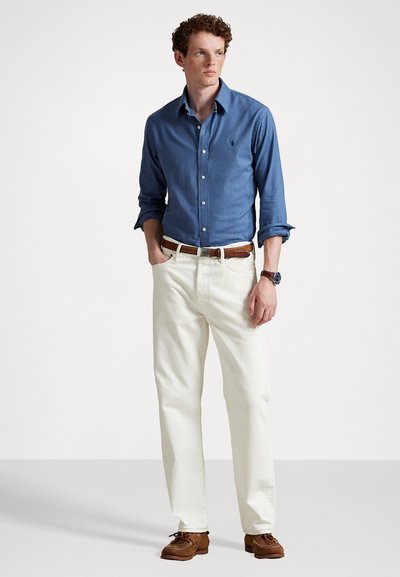 Cămașă din chambray bleu deschis, butonată, cu guler; pantaloni crem; curea din piele maro; pantofi maro; ceas clasic la încheietură.