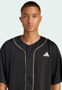 Čierna baseballová dres z sieťoviny, s krátkymi rukávmi, gombíkovým zapínaním a smotanovo bielym lemovaním. Biely logo na hrudi.