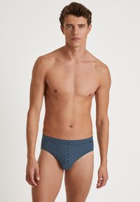 Herren-Badebrieftangas in Navyblau mit geometrischen Mustern. Hergestellt aus glattem Material, mit gefüttertem Vorderteil und elastischem Bund.