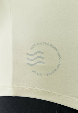 Lichtgroene sporttop met een gladde textuur, voorzien van een cirkelvormige afbeelding met de tekst "HOP ON THE BORN WAVE - NO WATER - NO US" en golvende lijnen.