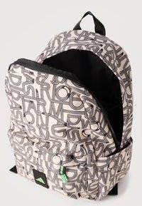 Μπεζ και μαύρο σακίδιο με σχέδιο, με μπροστινή τσέπη, μερικώς ανοιχτό κύριο χώρο, μαύρη λαβή και πράσινο τράβηγμα φερμουάρ.