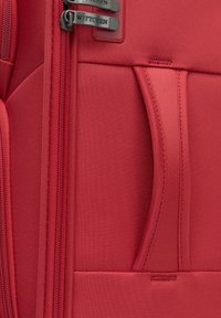 Rode stoffen koffer van duurzaam textiel met textuur, voorzien van een voorkantzak, dubbele ritsen met zwarte accenten en een merklogo-detail.