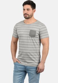 Grå stribet kortærmet t-shirt med rund hals og en kontrasterende grå brystlomme. Har en blød tekstur og en afslappet pasform.